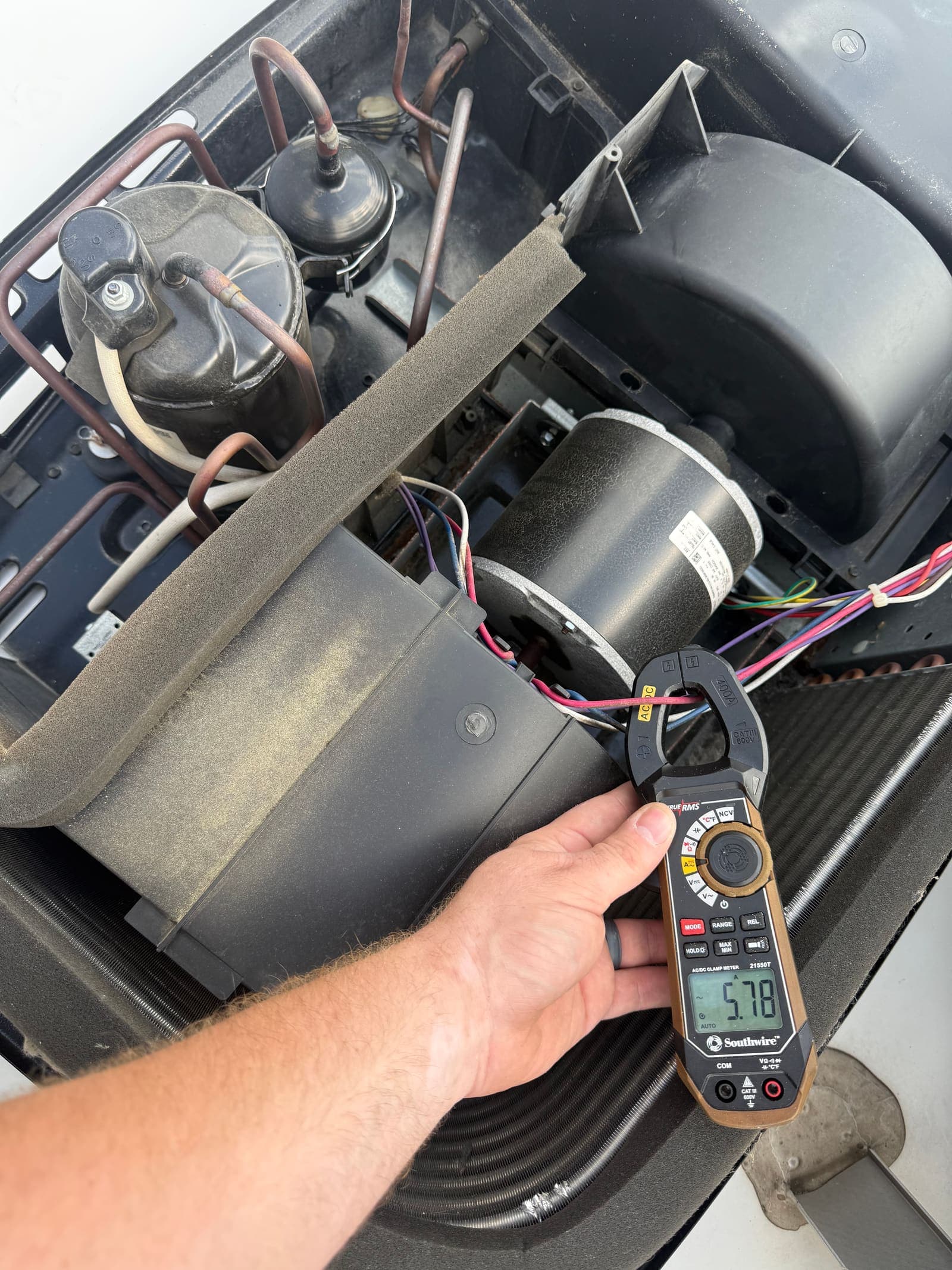 Technician testing RV rooftop air conditioner fan motor with a digital clamp meter