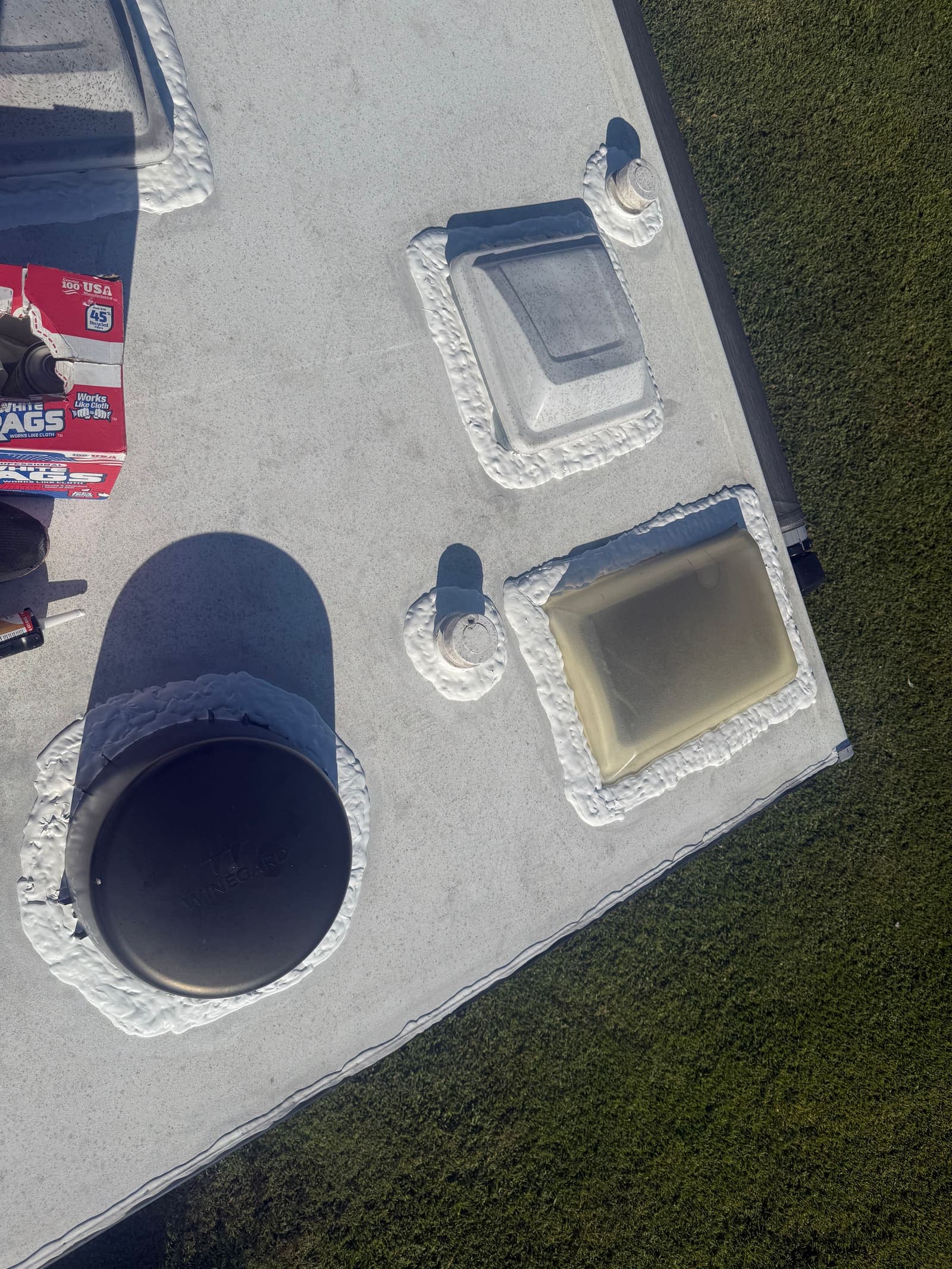 Fresh white lap sealant applied around RV roof vents and a Winegard antenna